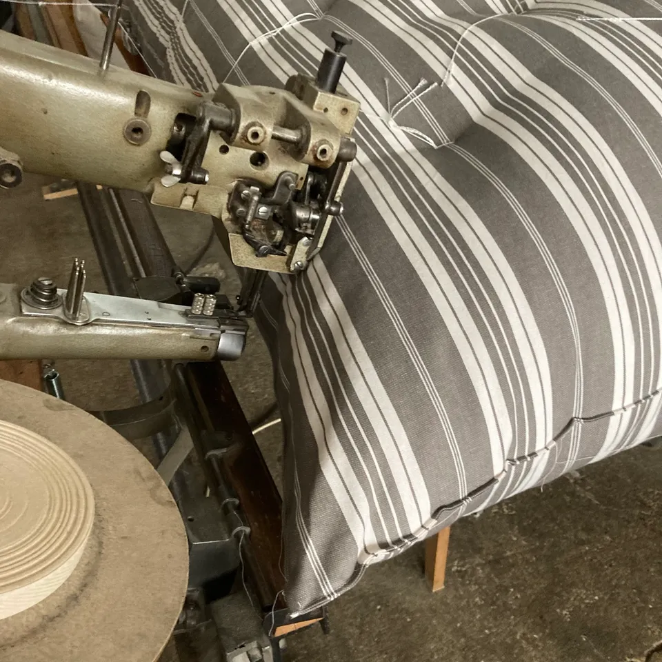 Tête de piqueuse en action sur la bordure d’un matelas à rayures grises