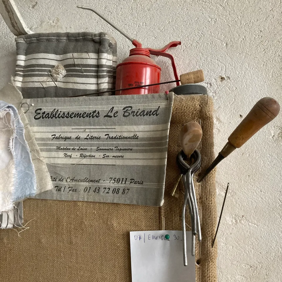 Outils de matelassier au mur : longues aiguilles, poinçon, burette et sacoche rayée