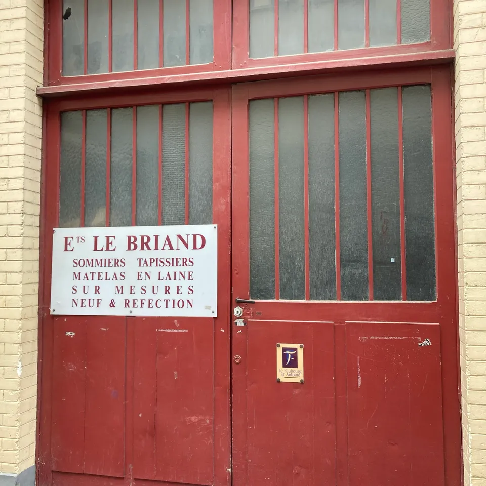 Porte d’atelier rouge et plaque « Ets Le Briand, sommiers tapissiers, matelas en laine »