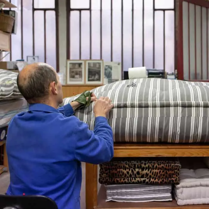Matelassier retravaillant un matelas en coutil rayé sur l’établi de l’atelier