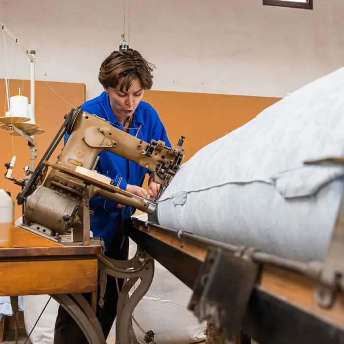 Matelassière cousant le bord d’un matelas en laine sur une machine à piquer industrielle