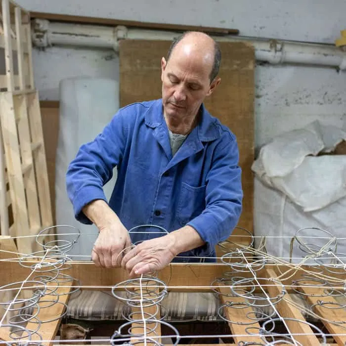Artisan montant les ressorts bi-coniques sur la caisse en bois d’un sommier tapissier