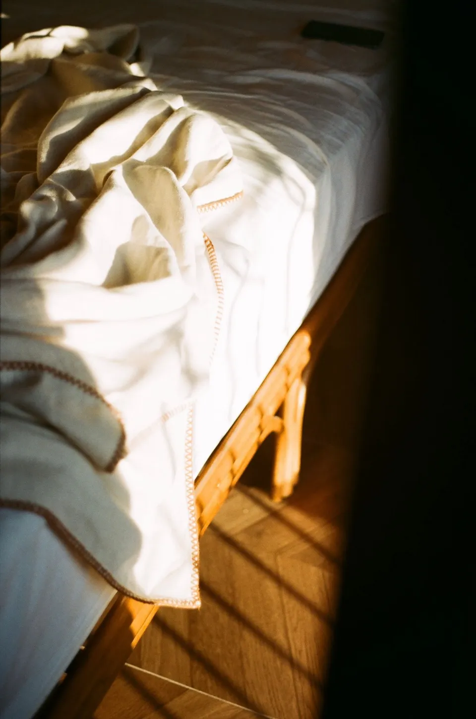 Coin d’un lit en bois, drap de lin froissé, dans la lumière du matin, sans oreiller
