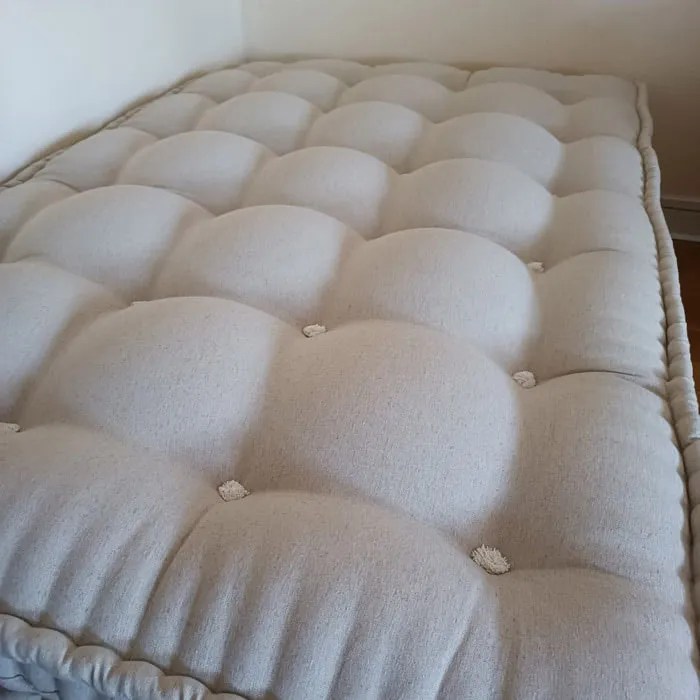 Surface bombée d’un matelas en laine écru, capitons et bouffettes vus de dessus