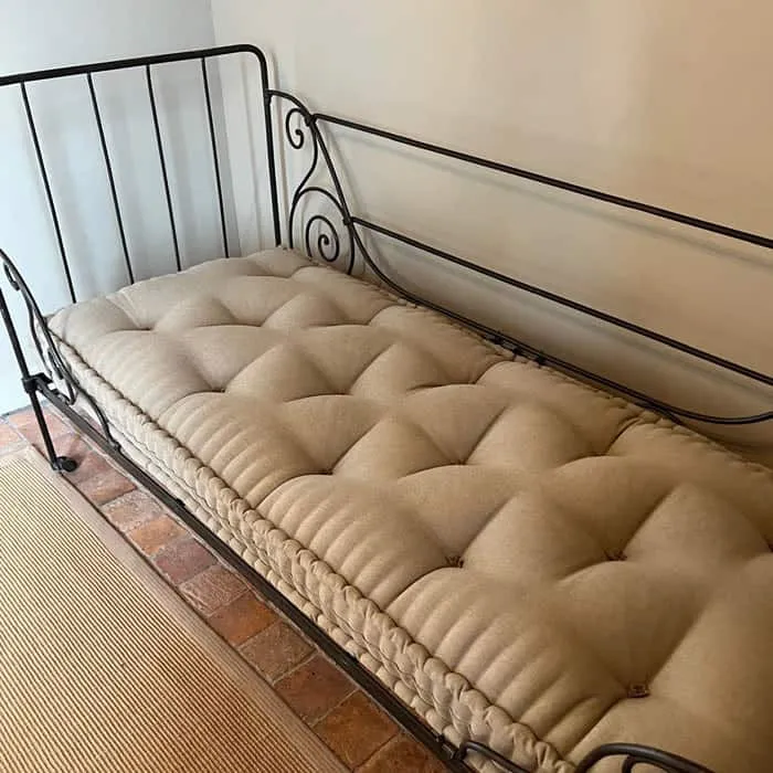 Matelas en laine capitonné beige posé sur un lit en fer forgé noir