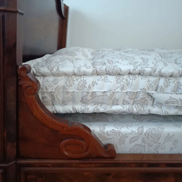 Matelas en laine vu de profil sur un lit ancien en bois sculpté, épaisseur du capitonnage visible