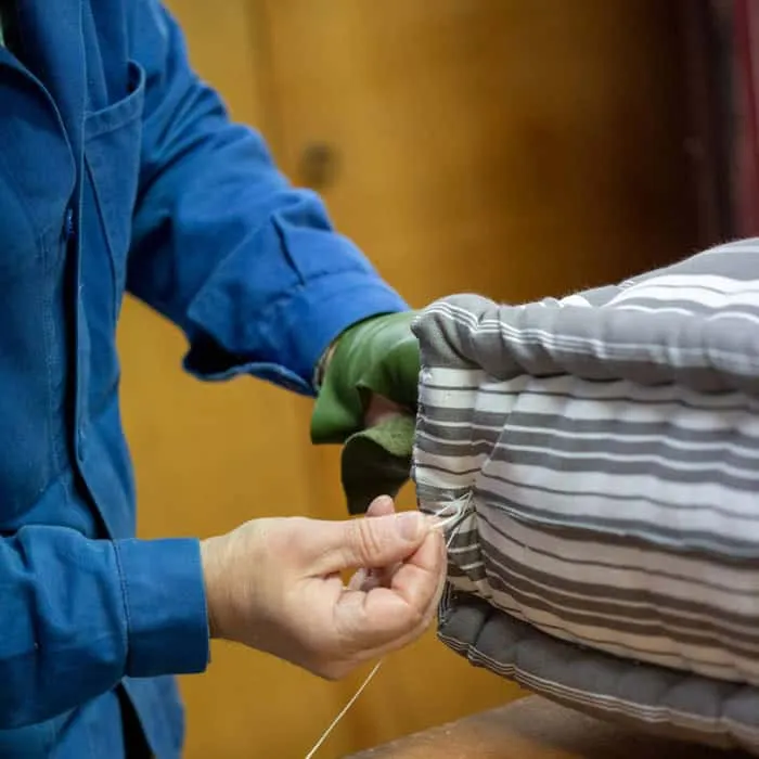 Matelassier au travail, aiguille en main, sur le bourrelet d'un matelas rayé