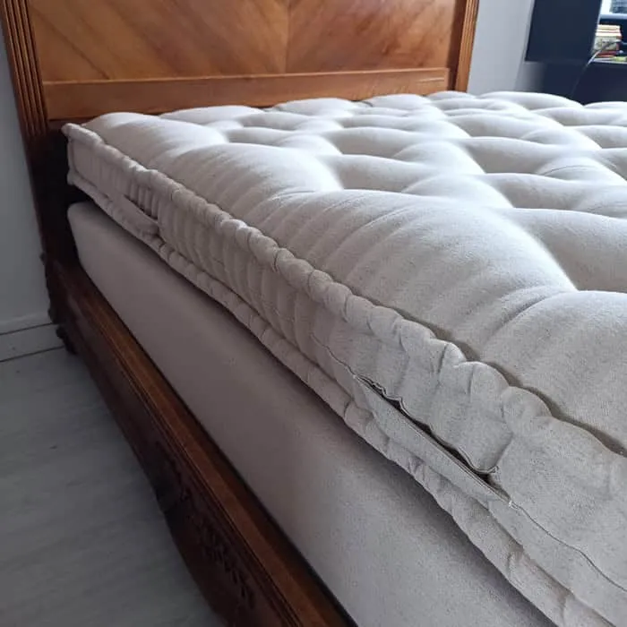 Matelas en laine écru posé sur son sommier dans un lit ancien en bois