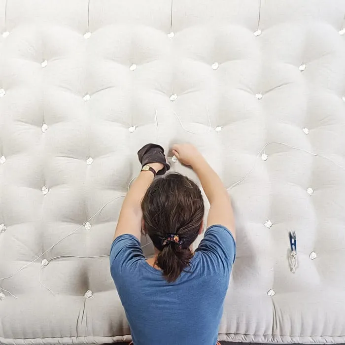 Mains nouant les fils des capitons sur une grande surface de matelas blanche