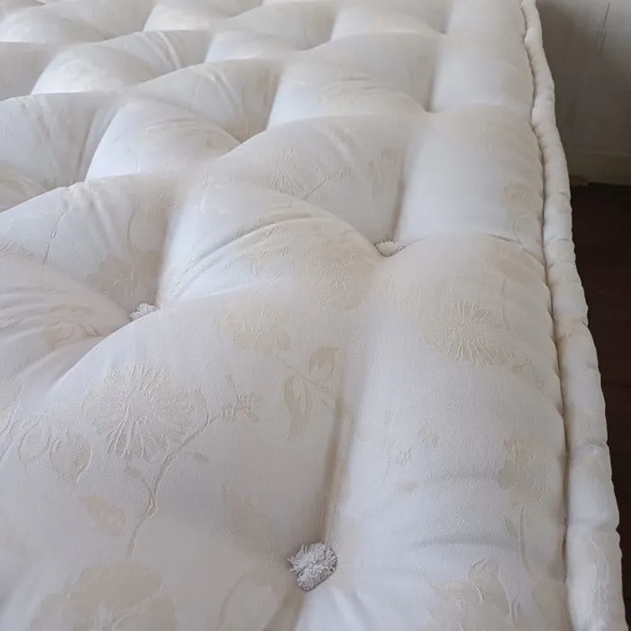 Matelas neuf vu de son coin : damassé crème, capitons alignés, bourrelet fini