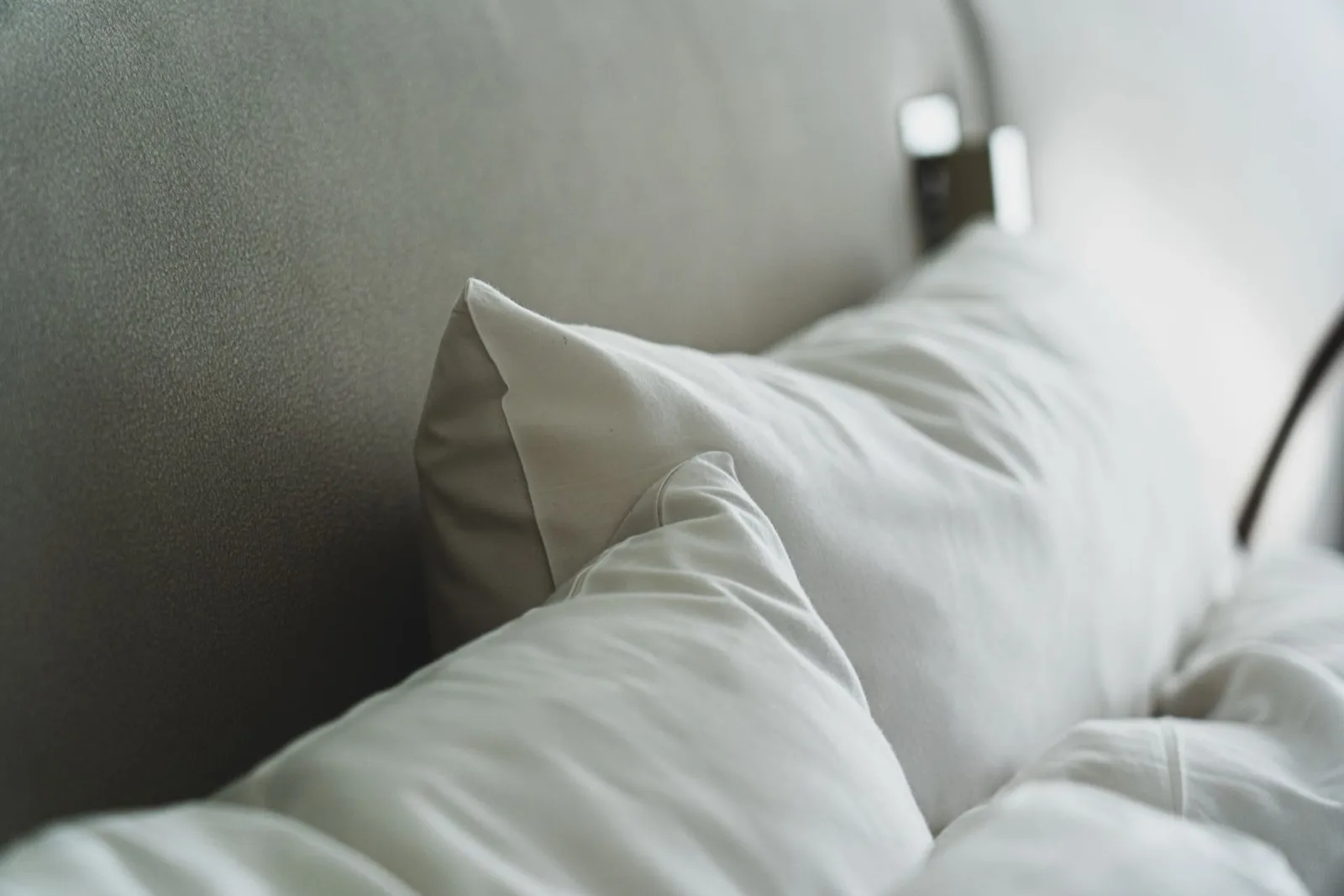Oreillers blancs sans taie appuyés contre une tête de lit sombre