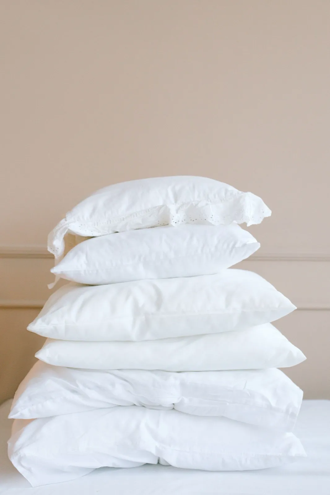 Pile de six oreillers blancs de formes et de tailles différentes sur un lit