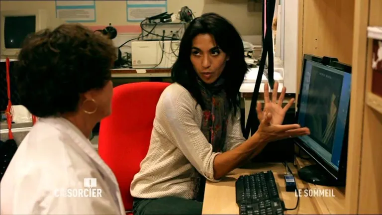 Dans un laboratoire du sommeil, une chercheuse commente un tracé affiché à l'écran devant une collègue en blouse blanche.